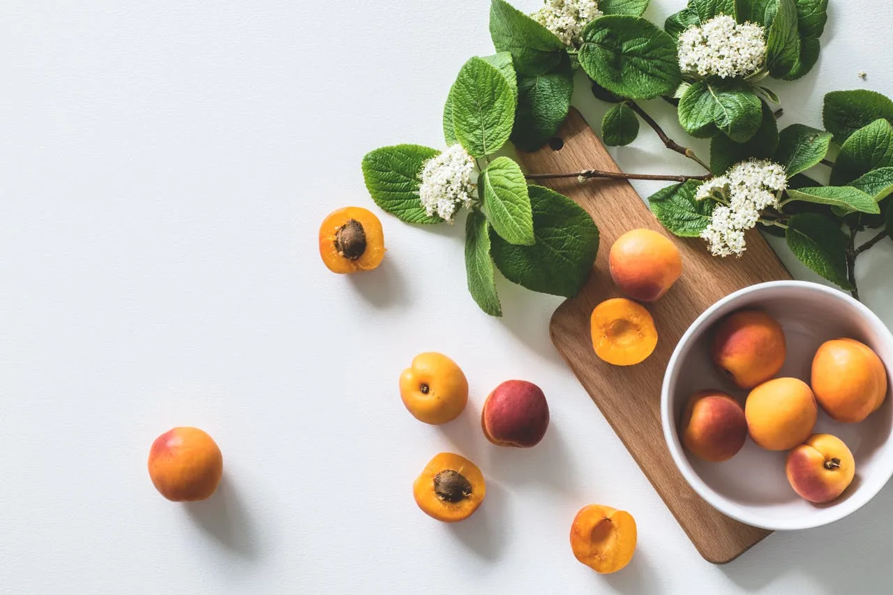 gallery-1 A bright still life of fresh apricots and blossoms on a cutting board, perfect for healthy eating.